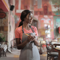 Junge Frau arbeitet in einem Restaurant. Sie sieht sehr zufrieden aus, lächelt und hält einen Block und einen Stift in der Hand.